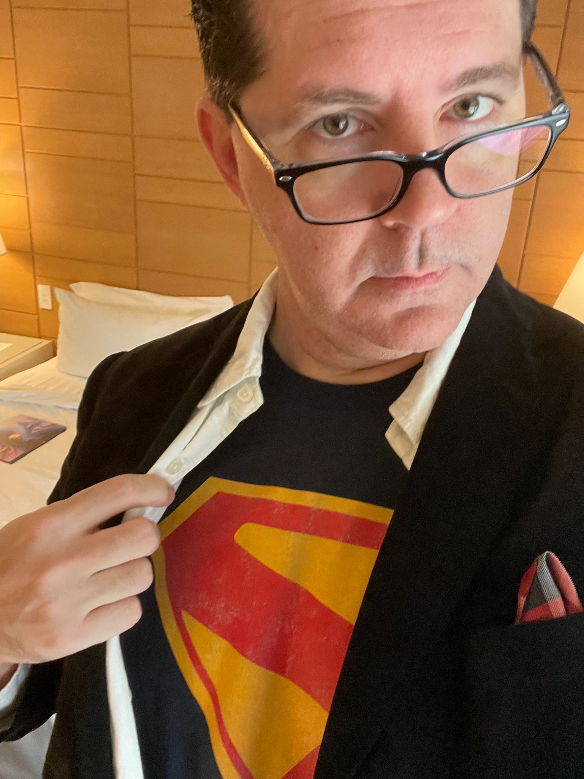 A close-up of a man in a sport coat revealing a Superman logo shirt underneath.