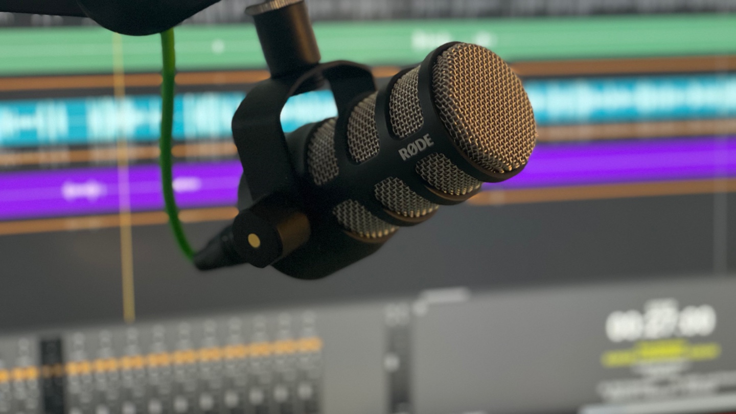 Image of a microphone on a boom stand with a screen of audio signals in the background.